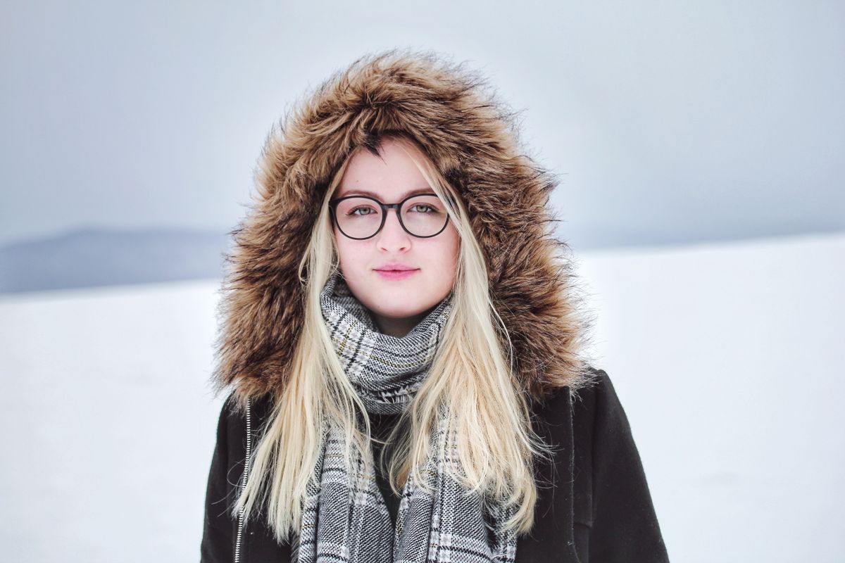 Portrait of a young woman outdoors in winter, wearing glasses and a fur-lined hooded coat.
