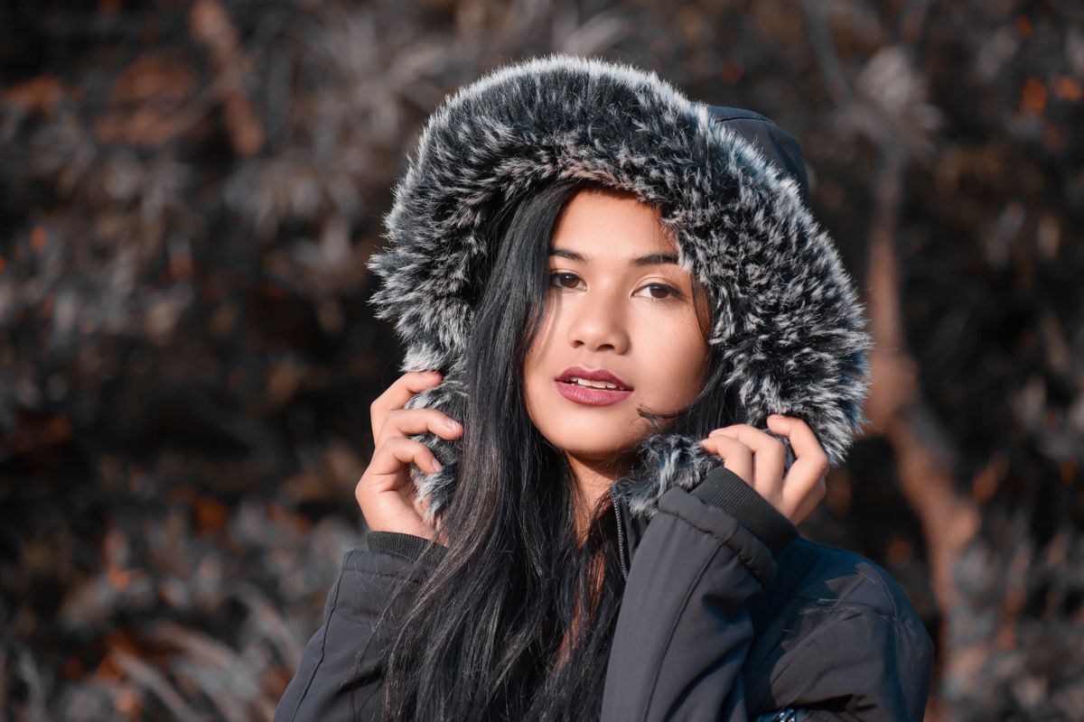 Portrait of a young woman wearing a faux fur hooded coat against an outdoor backdrop.