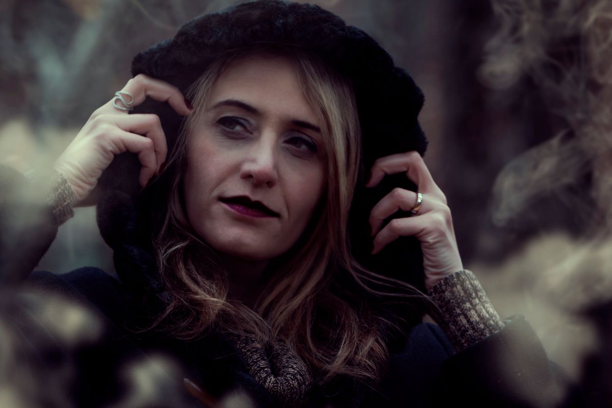 Portrait of a woman in a black hooded coat amidst foggy forest background.