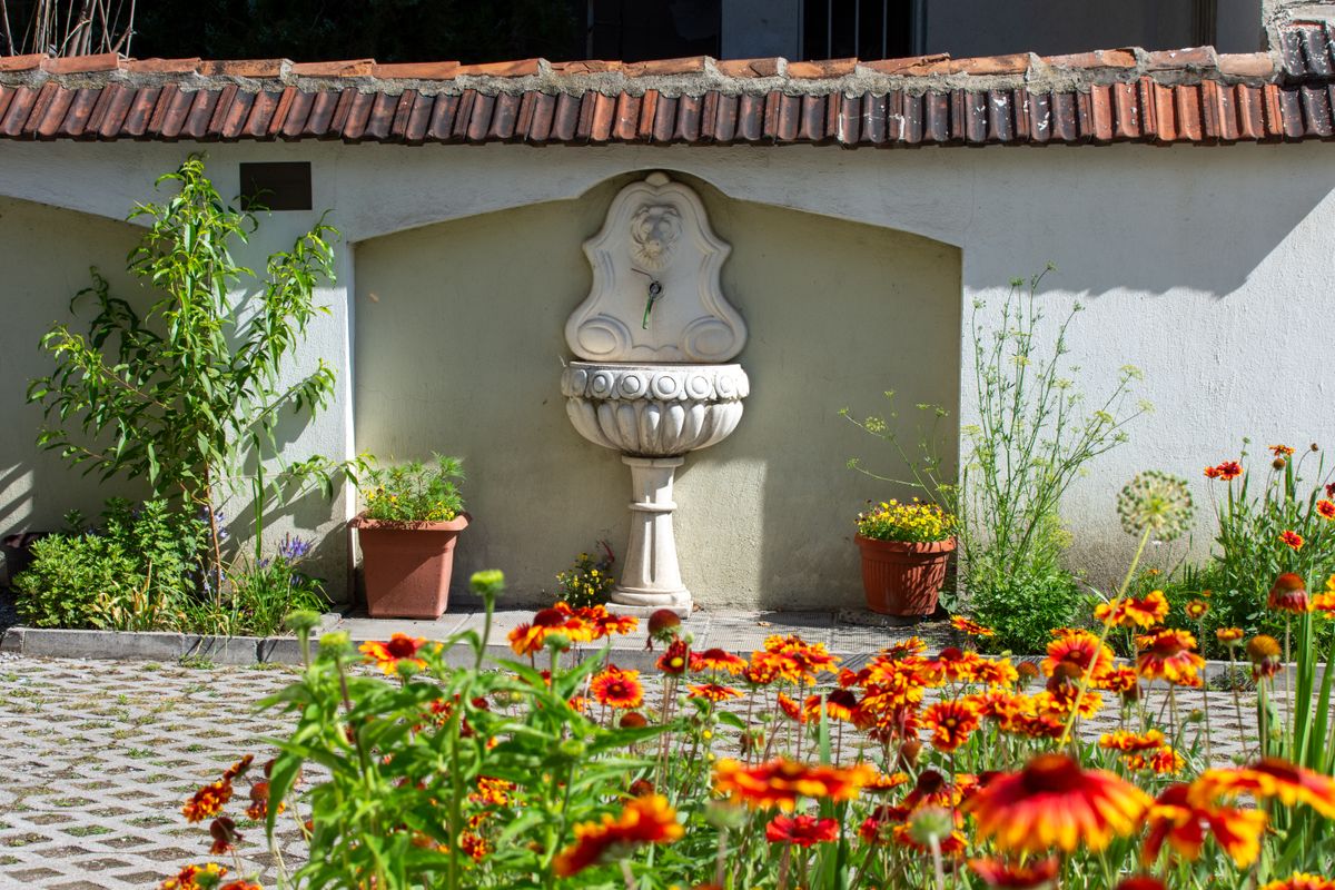A quaint garden scene with a decorative fountain and vibrant flowers under bright sunlight.