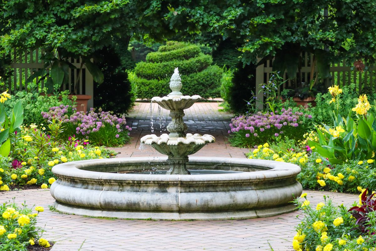 Serene garden fountain surrounded by vibrant flowers and lush greenery during the day.