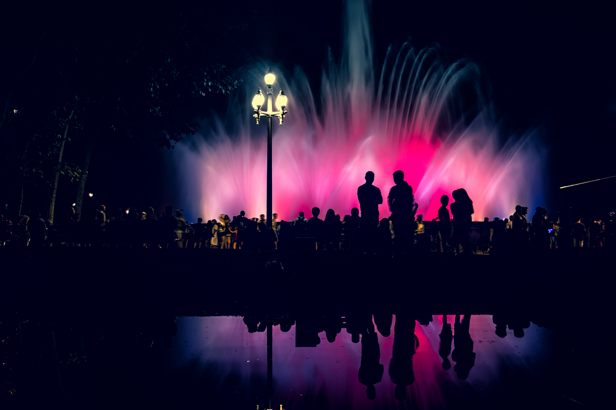 Silhouetted crowd at the vibrant Magic Fountain in Barcelona, with colorful water displays at night.