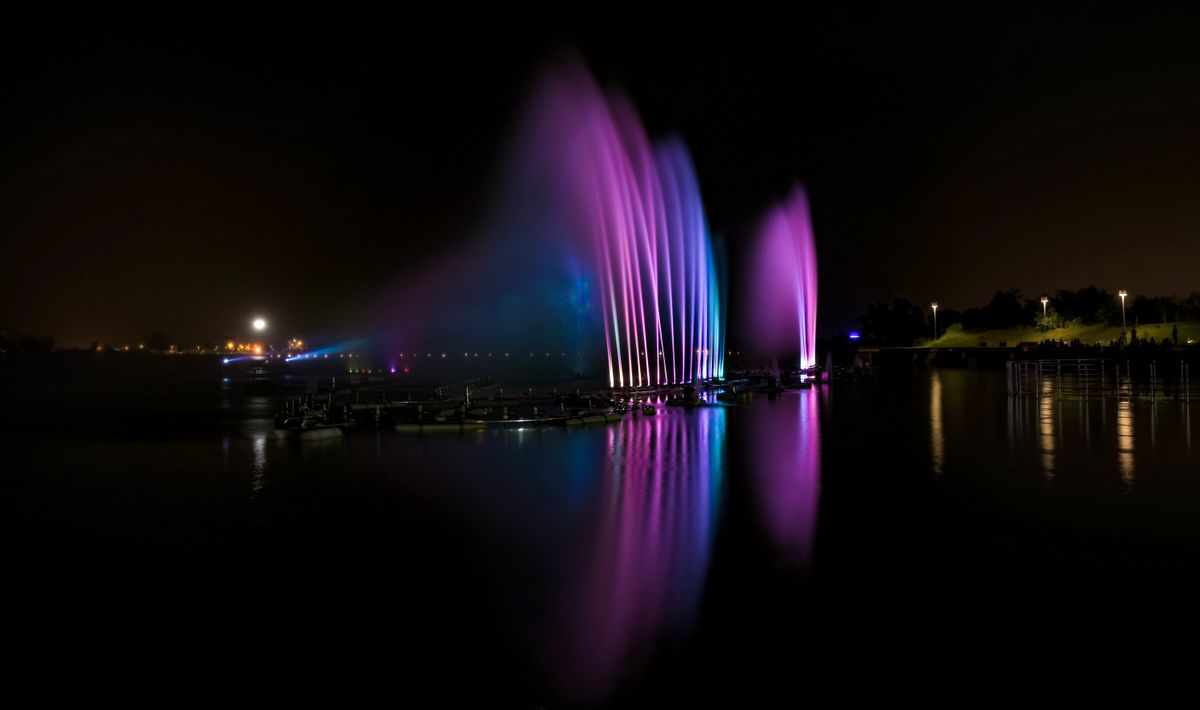 Colorful lights illuminate a water fountain at night, reflecting vividly on the river.