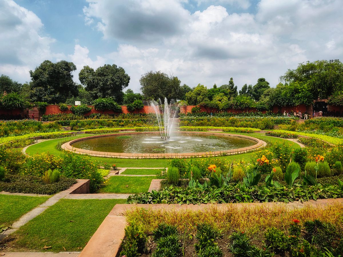 Tranquil garden scene featuring a vibrant circular fountain surrounded by lush greenery and blooming flowers.