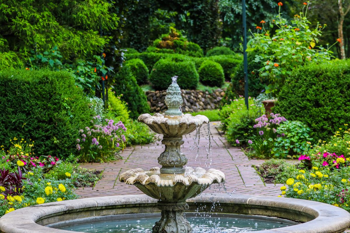 A tranquil garden scene featuring a classic stone fountain surrounded by lush greenery and colorful flowers.