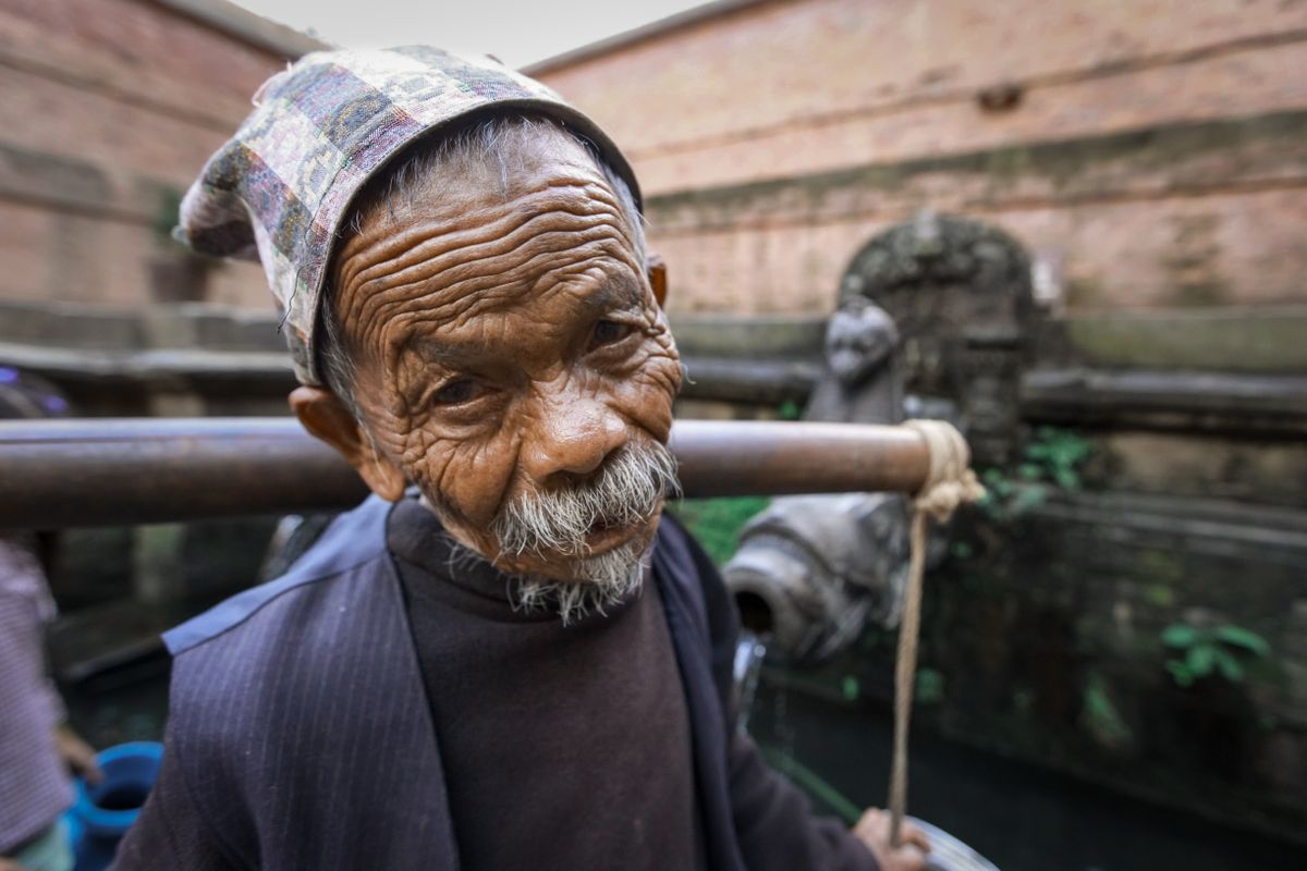 Close-up of an elderly man with facial hair at a traditional water fountain, outdoors.