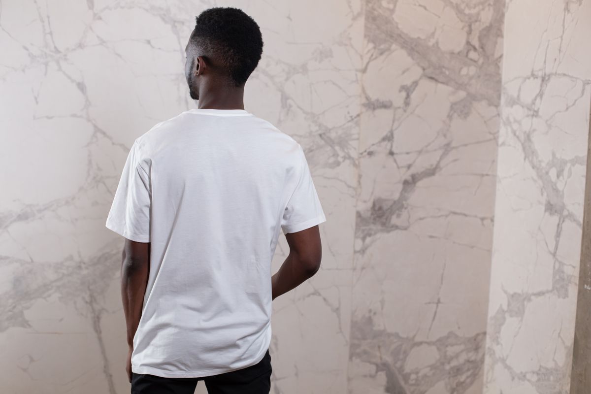 Back view of unrecognizable African American male wearing white t shirt and pants standing with hand in pocket