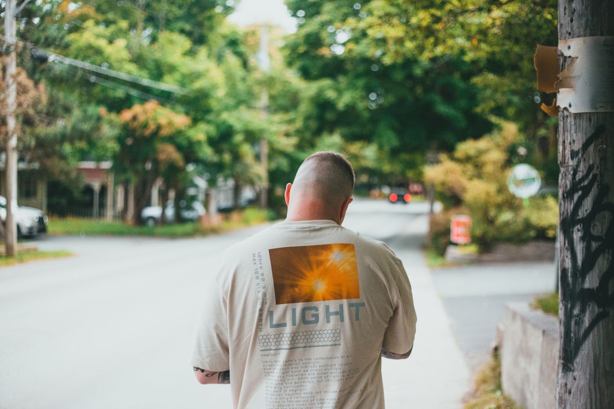 Man walking on sidewalk, wearing t-shirt with 'LIGHT' print, during a bright summer day.