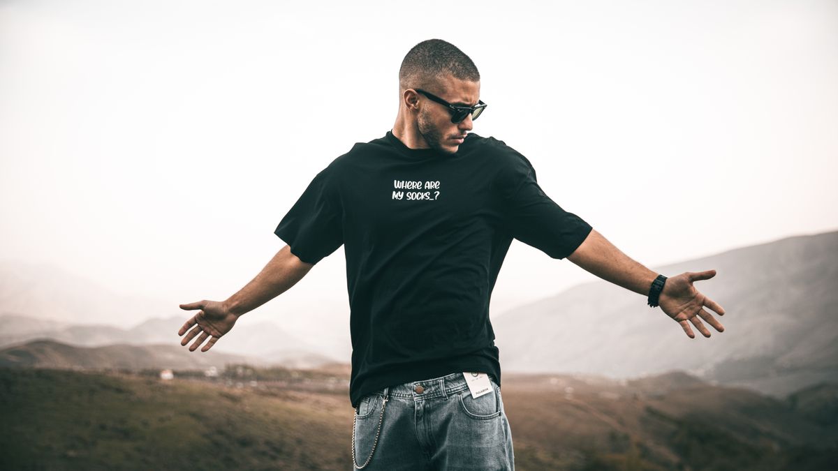 Fashionable young man posing confidently outdoors in Iran wearing sunglasses and graphic t-shirt.