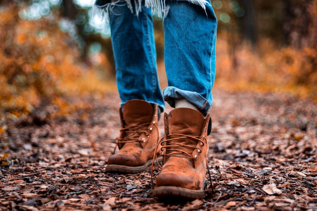 Close-up of rugged boots and jeans walking on a leafy autumn forest path.