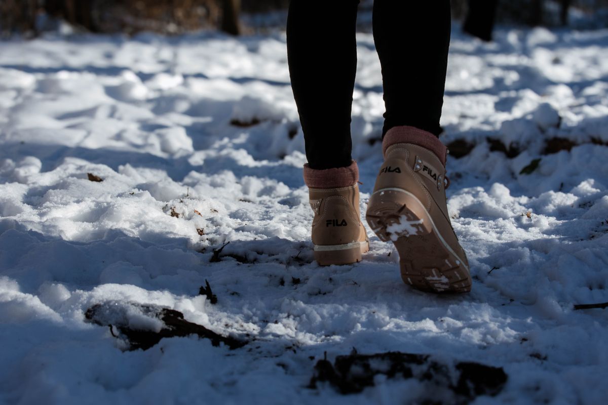 Person walking in brown boots on a snow-covered forest path, captured from behind.