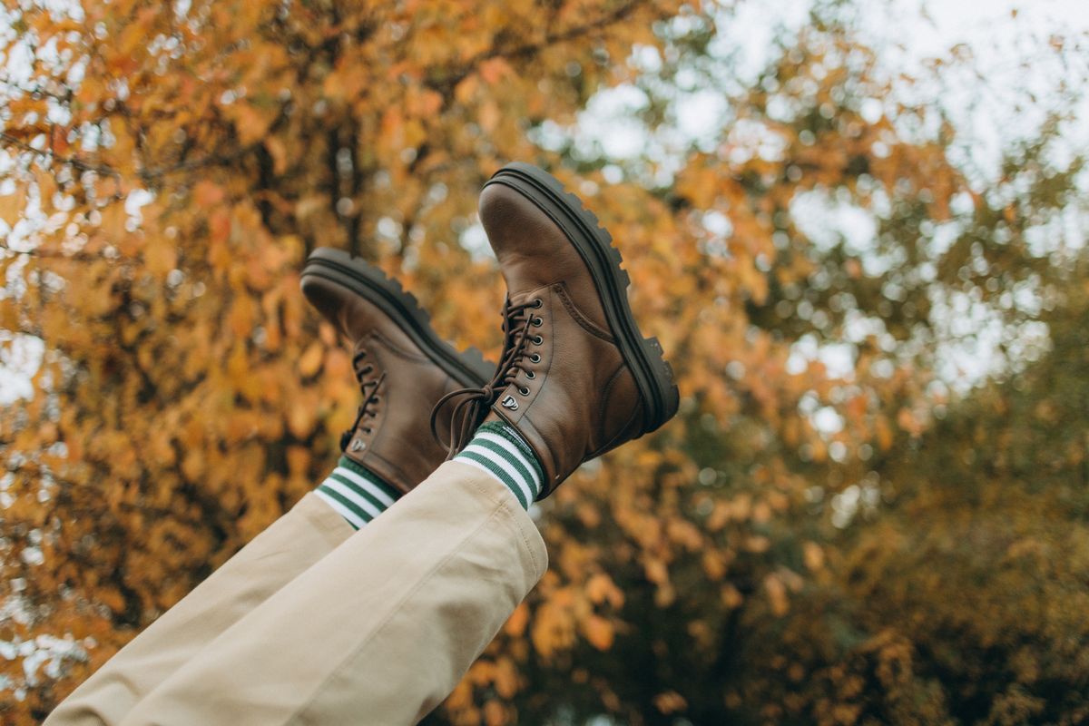 A pair of brown boots with striped socks against fall foliage.