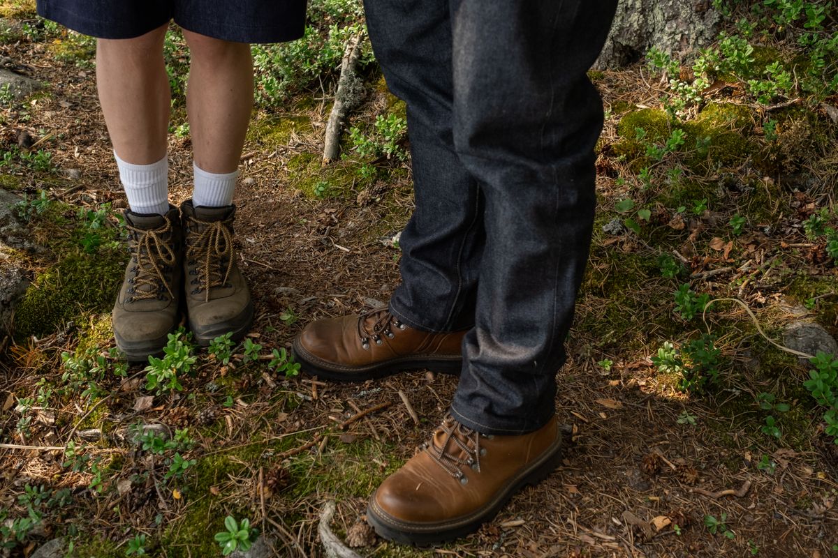 Close-up of two people wearing hiking boots in a forest setting.
