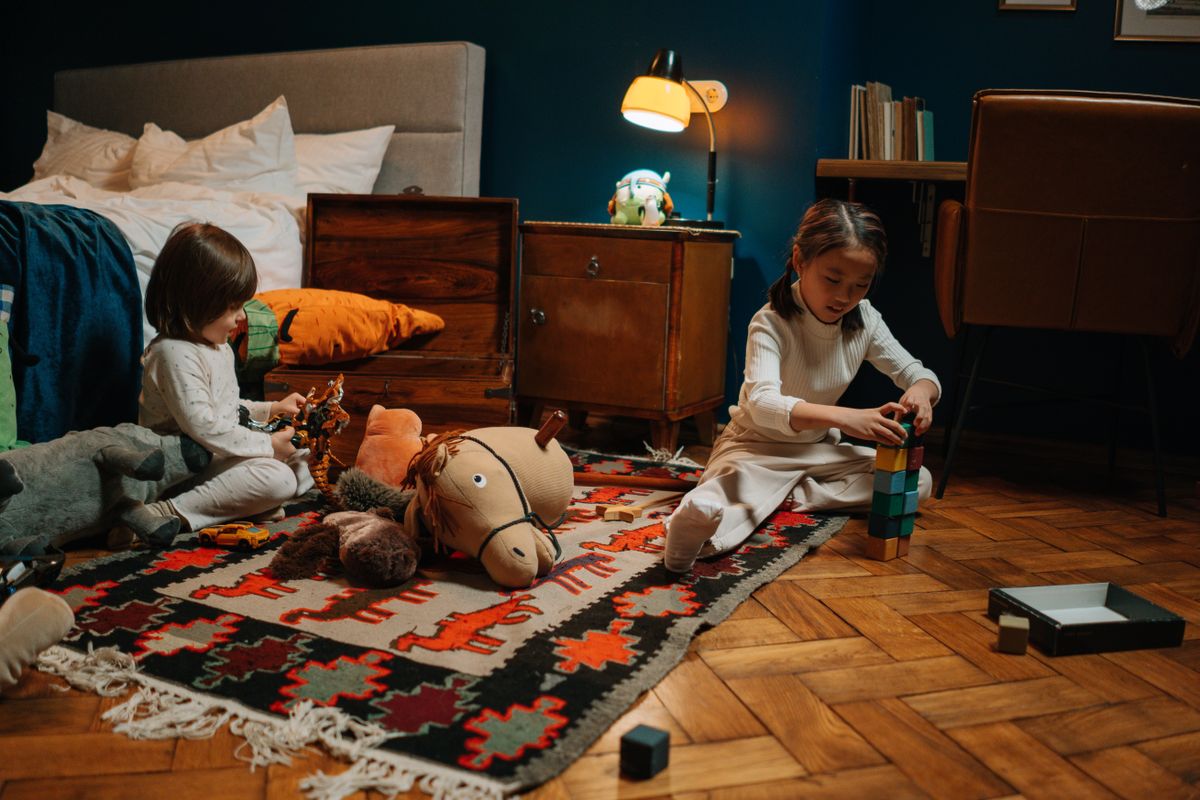 Two children in pajamas play with toys in a warmly lit bedroom, creating a joyful scene.