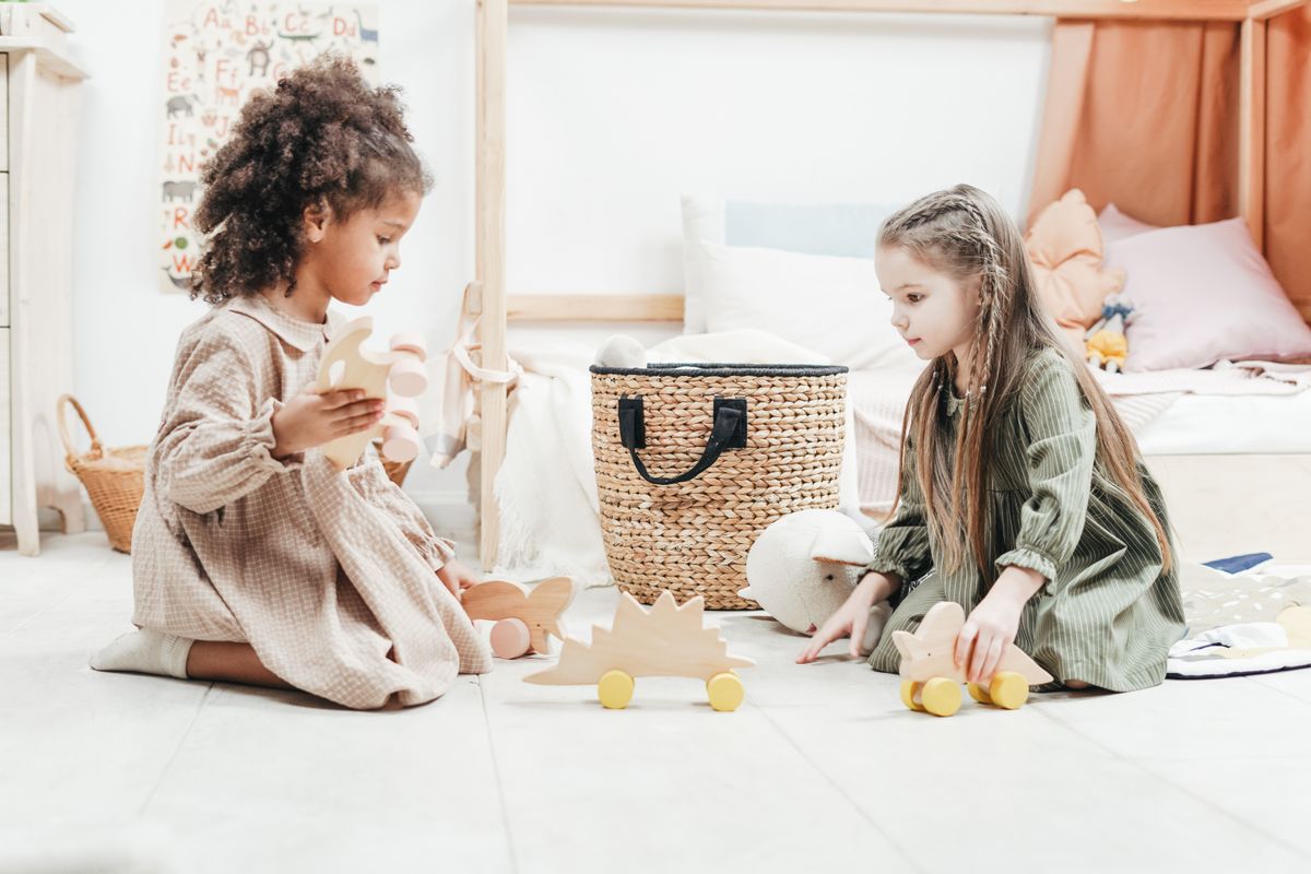 Two young girls enjoy playing with wooden toys in a cozy indoor playroom setting.