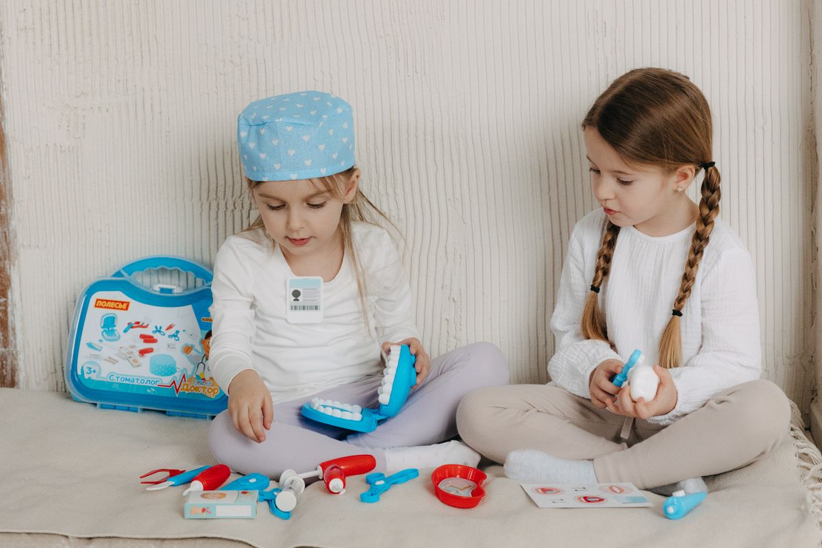 Two young girls role-playing as dentists with a toy dental kit indoors.