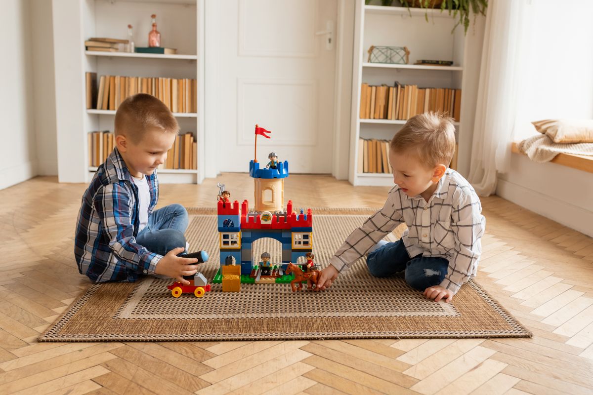Two young boys enjoying building a colorful toy castle indoors with plastic blocks.