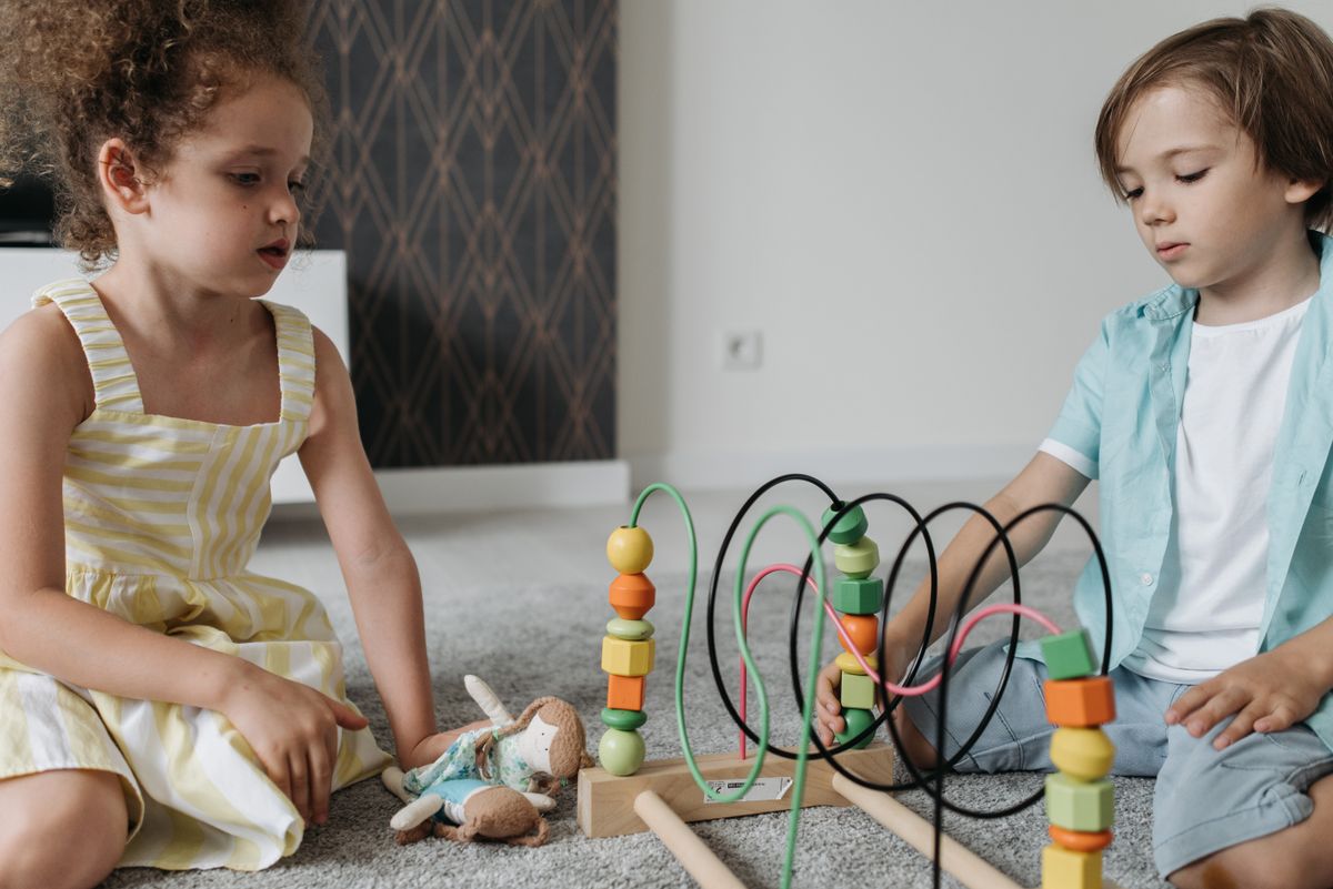 Kids engaging with colorful bead maze toy on carpet, promoting cognitive skills.