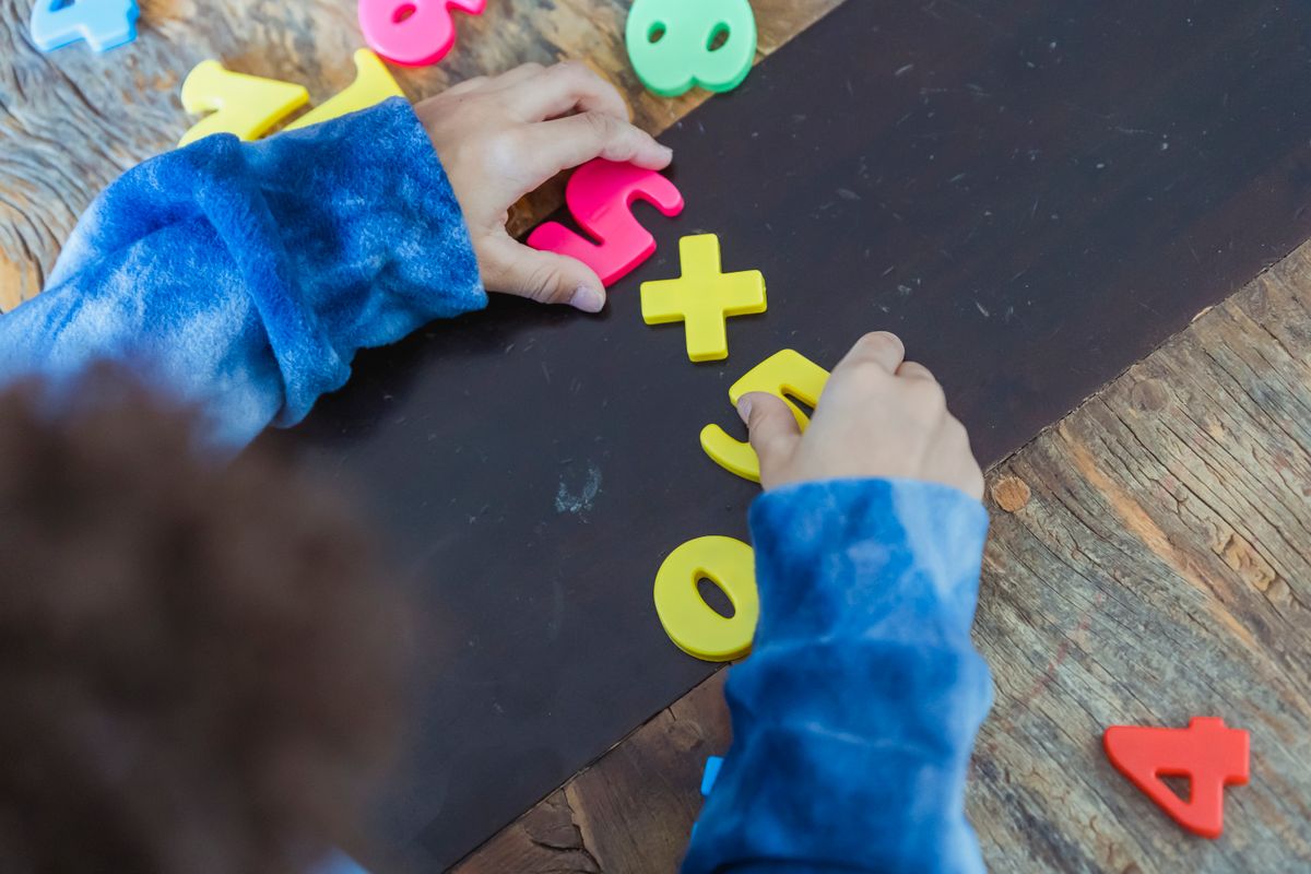 High angle of crop anonymous ethnic kid making mathematical multiplication with colorful plastic numbers during learning process