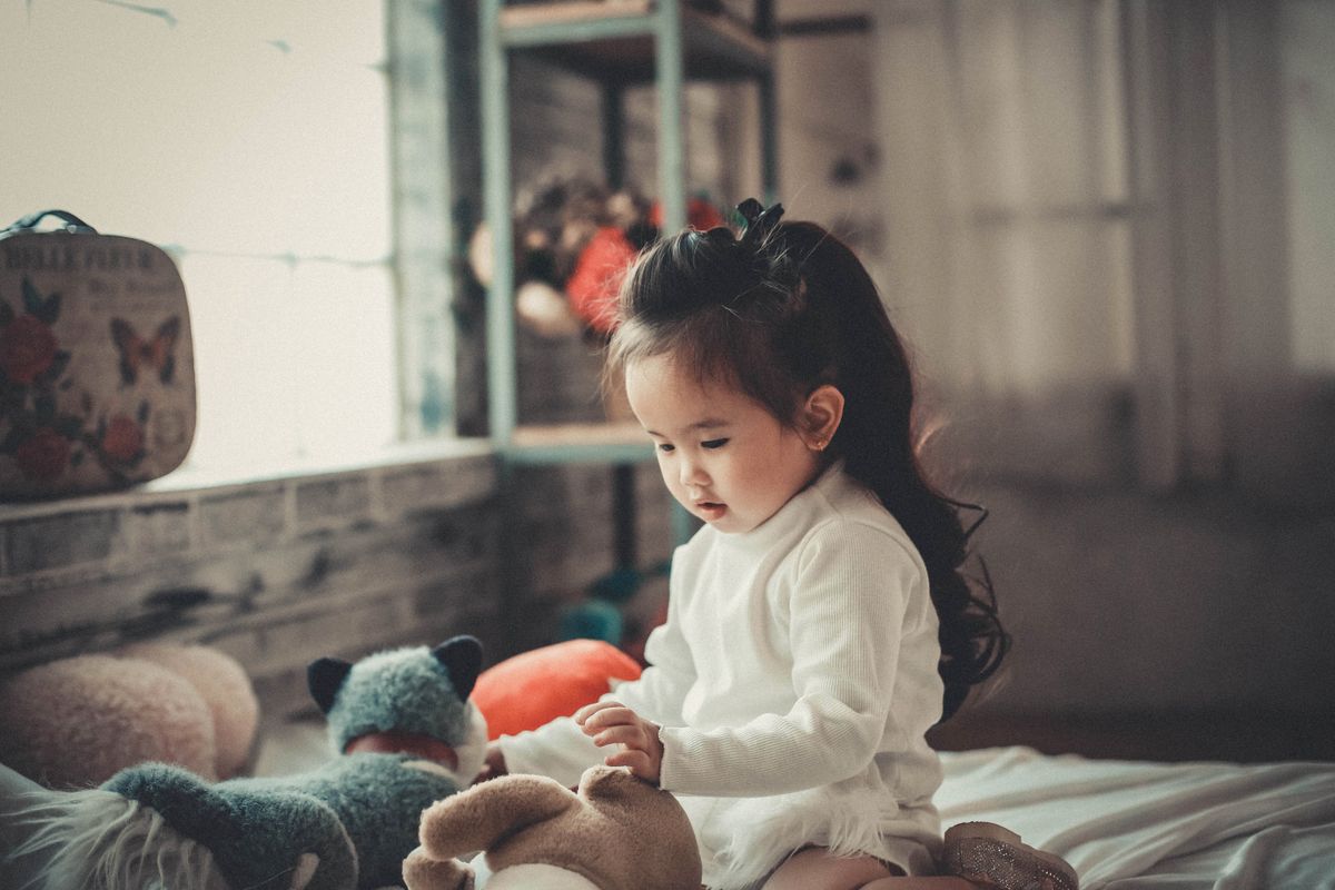 Adorable Asian child playing with stuffed toys indoors, showcasing innocent childhood moments.