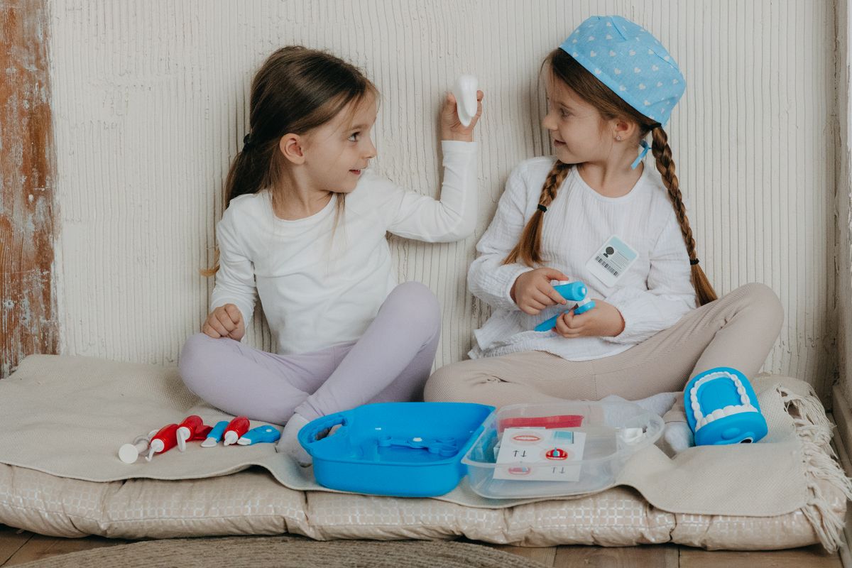 Two young girls playing dentist with a toy kit in a cozy indoor setting, sharing smiles and fun.