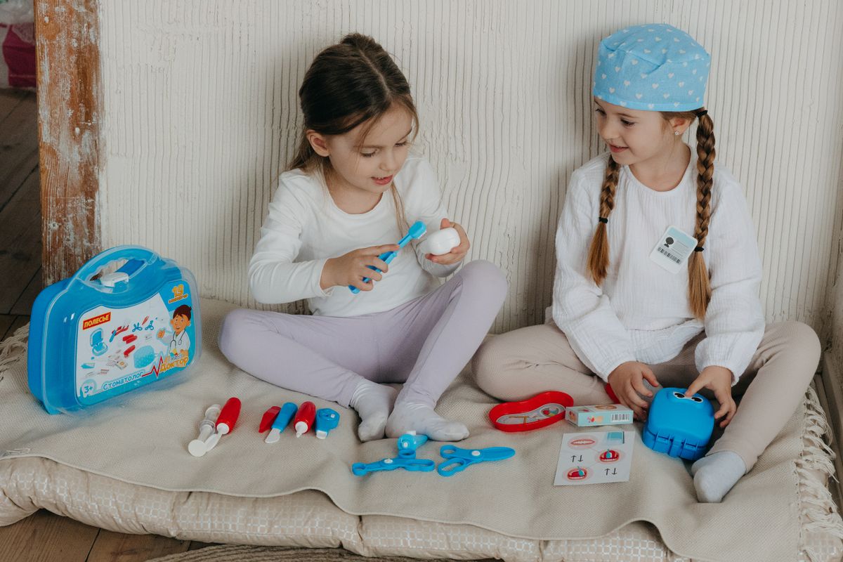 Two young girls playing doctor with a toy medical kit indoors, fostering creativity and imagination.