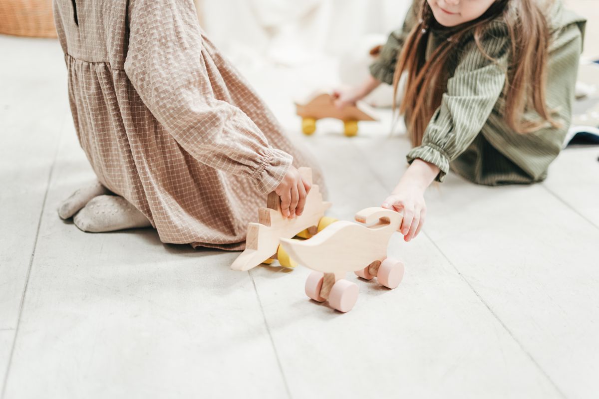 Two children enjoy playing with wooden dinosaur toys indoors, capturing the joy of childhood.