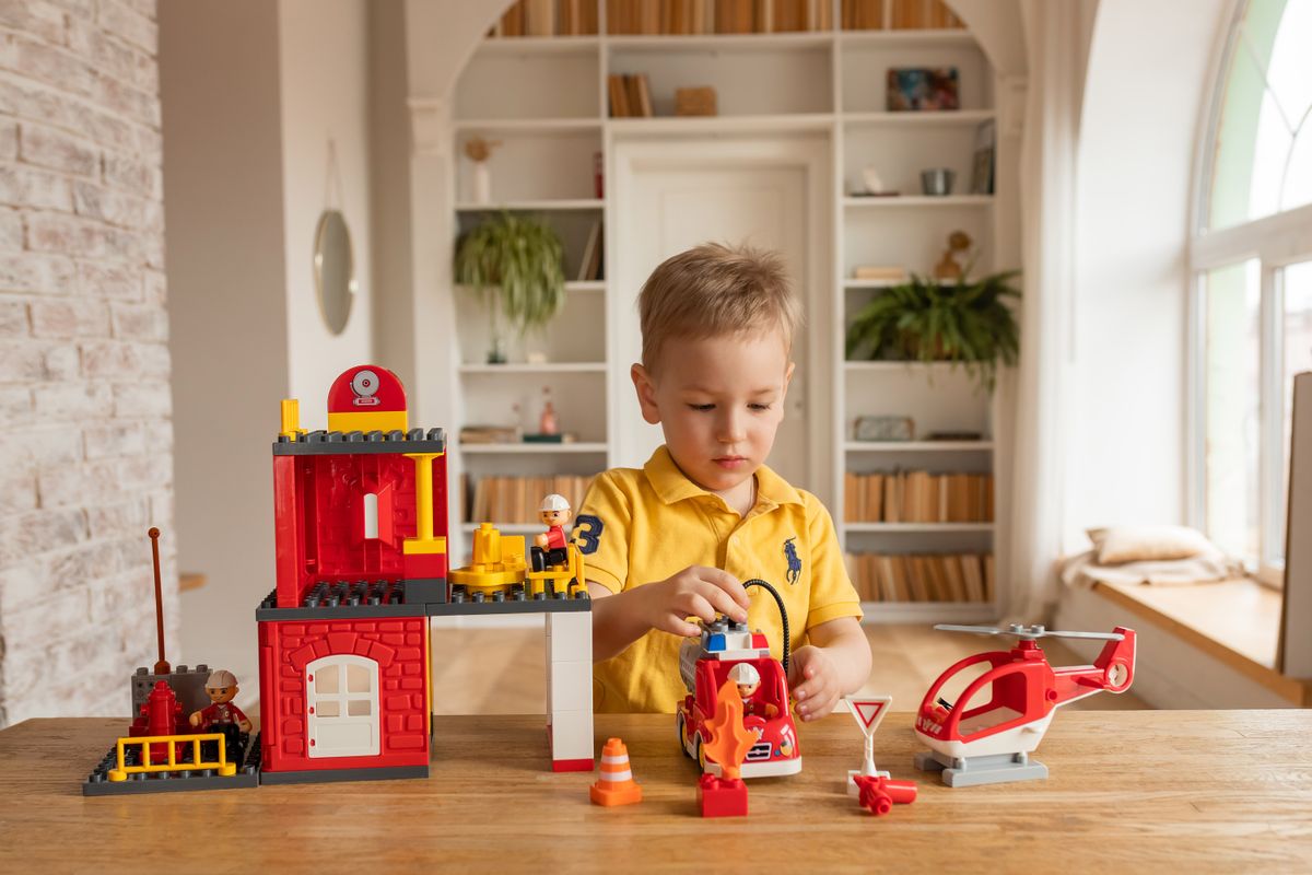 Young boy enjoys playing with toy fire station set indoors, promoting creativity and imagination.