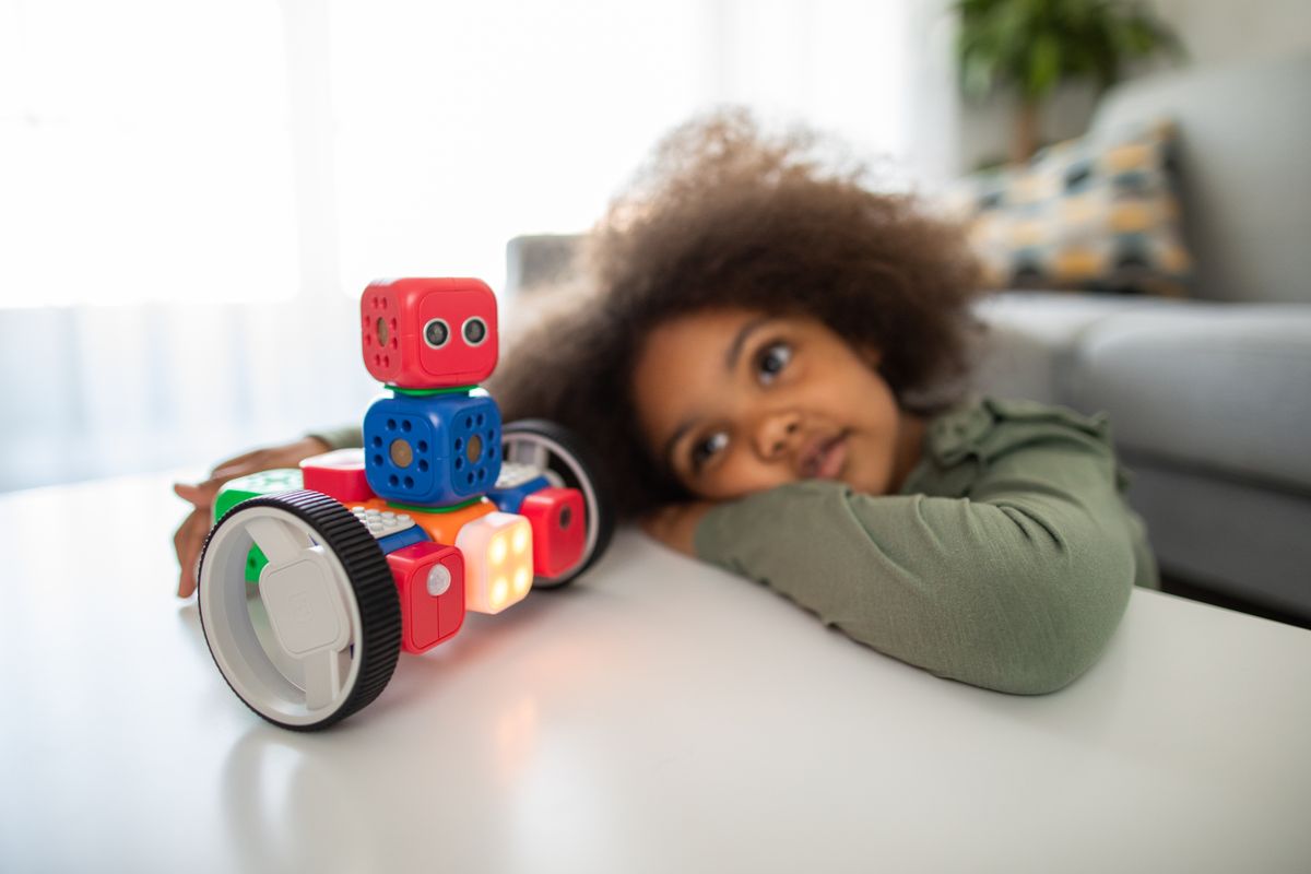 African American girl with afro hair playing with a colorful robot toy indoors, relaxed mood.
