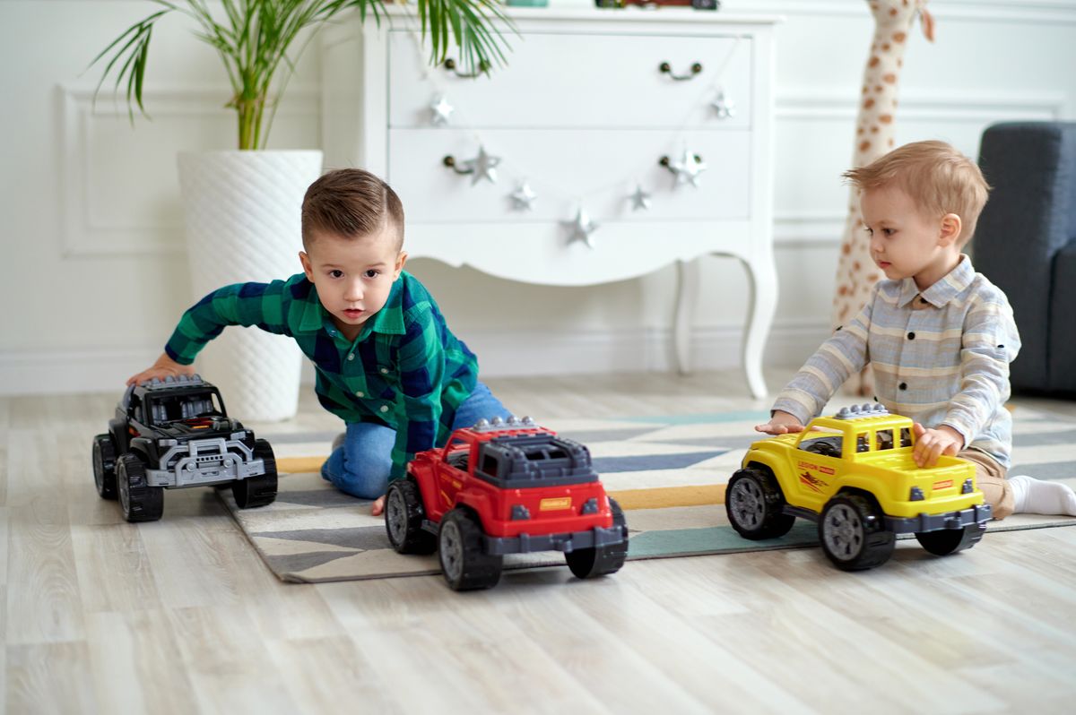Two young boys playing with colorful toy cars on the floor indoors.