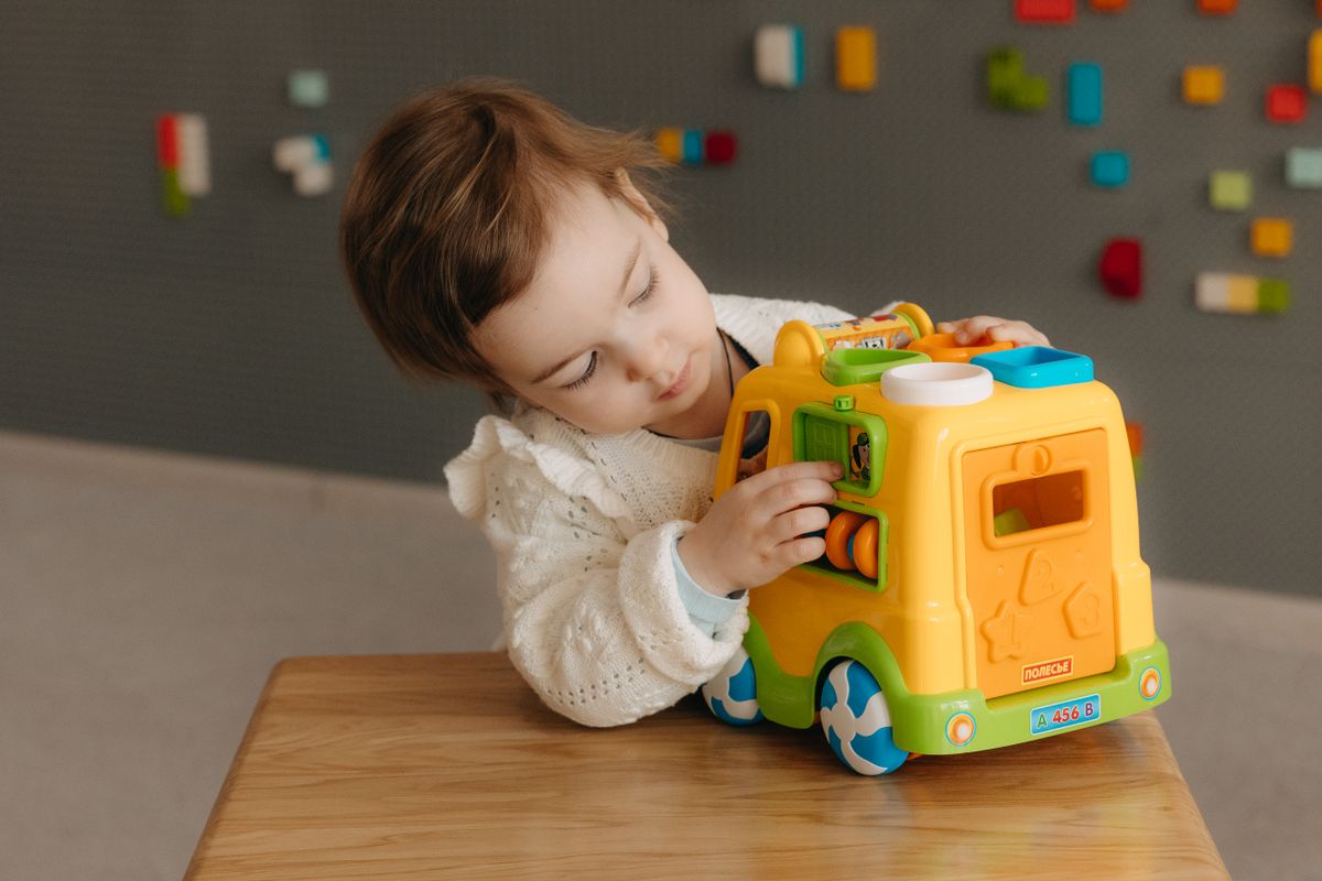Young child playing with a colorful toy bus, fostering creativity and curiosity indoors.