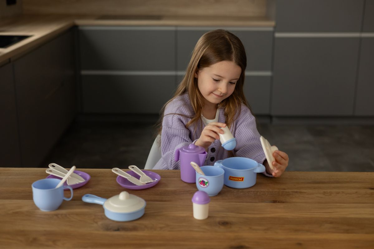 A young girl enjoys playtime with colorful toy tableware in a modern kitchen setting.