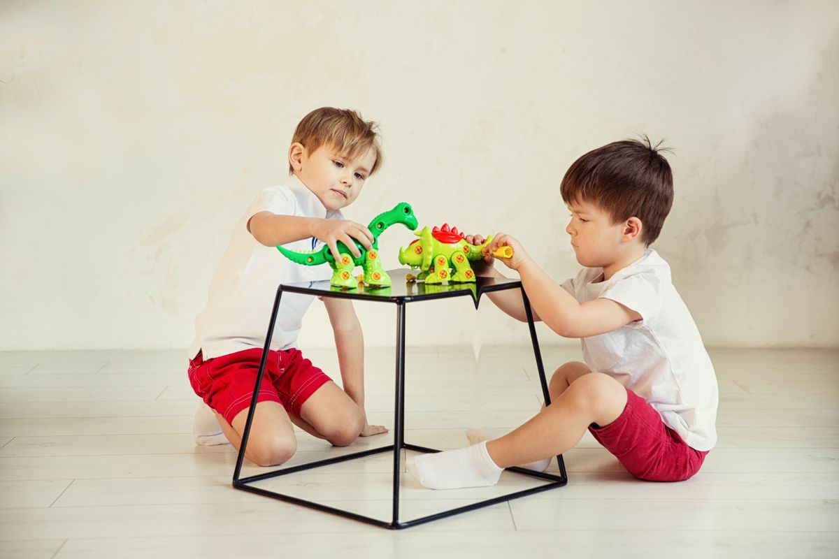 Two kids enjoy playing with dinosaur toys indoors, fostering creativity and imagination.