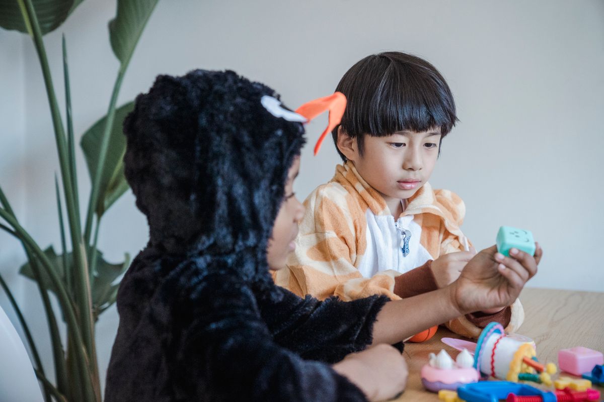 Two kids in playful animal onesies engage in a fun indoor activity with toys on a table.