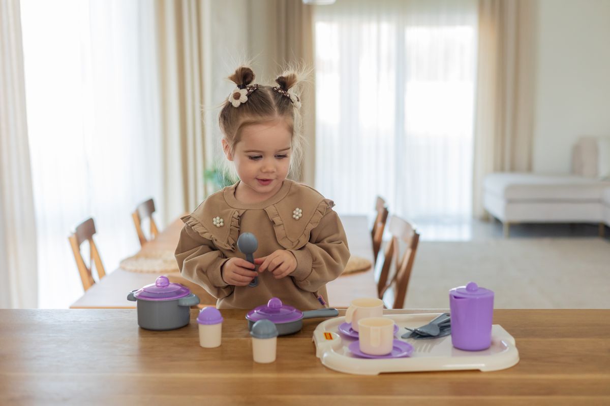 Little girl enjoying imaginative play with toy kitchen set in a cozy, well-lit room.