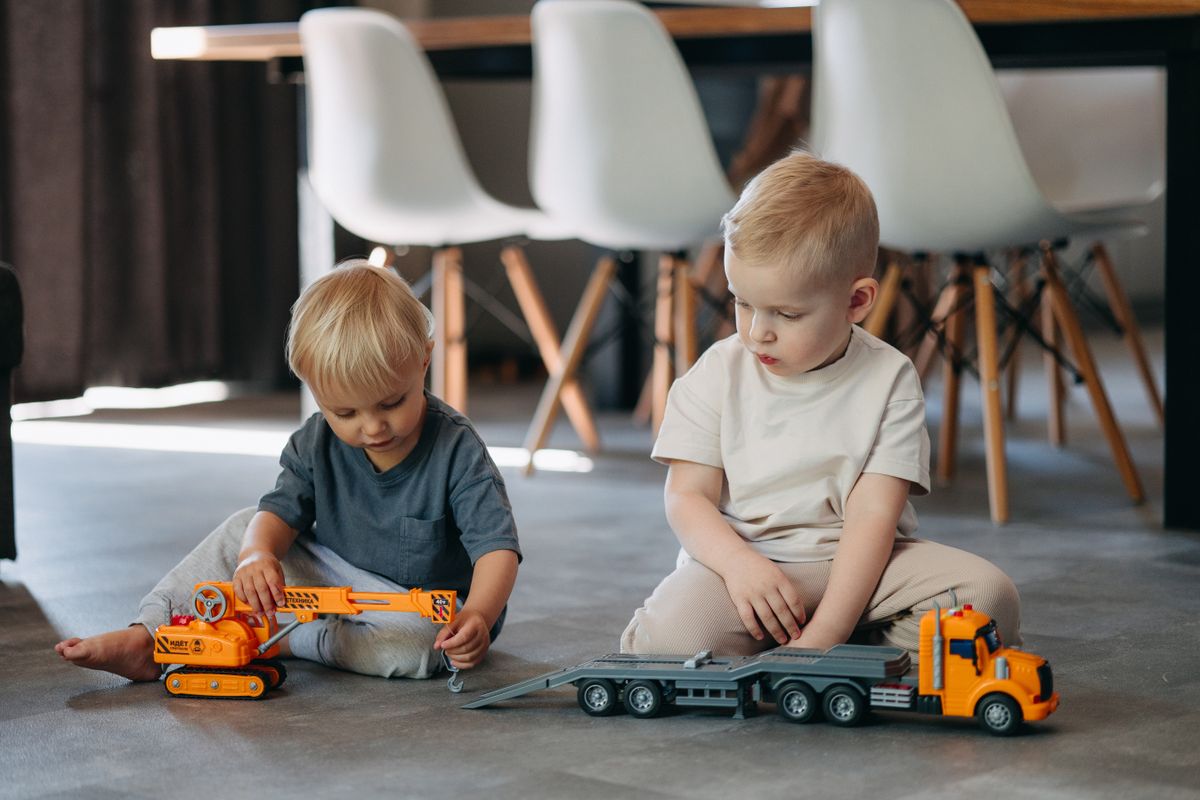 Two young boys play with toy trucks indoors, enjoying imaginative playtime.