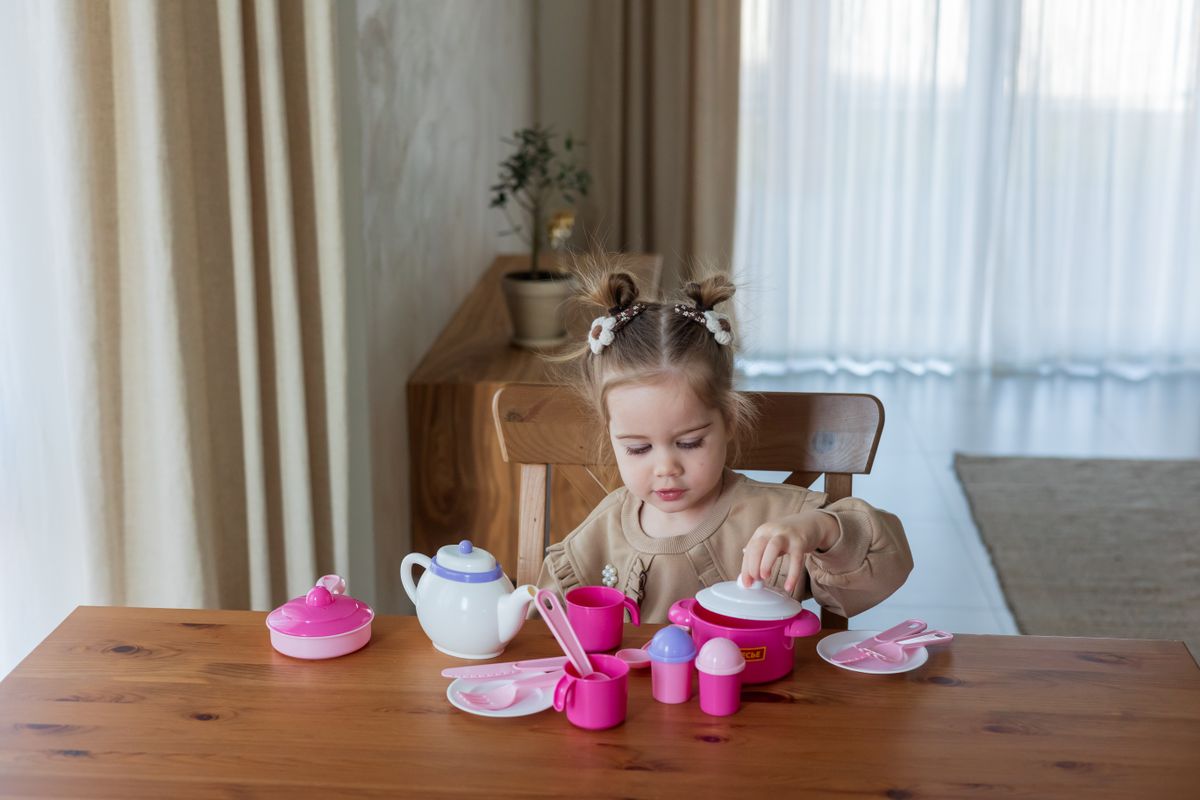 Young child playing a pretend tea party indoors with pink tableware.