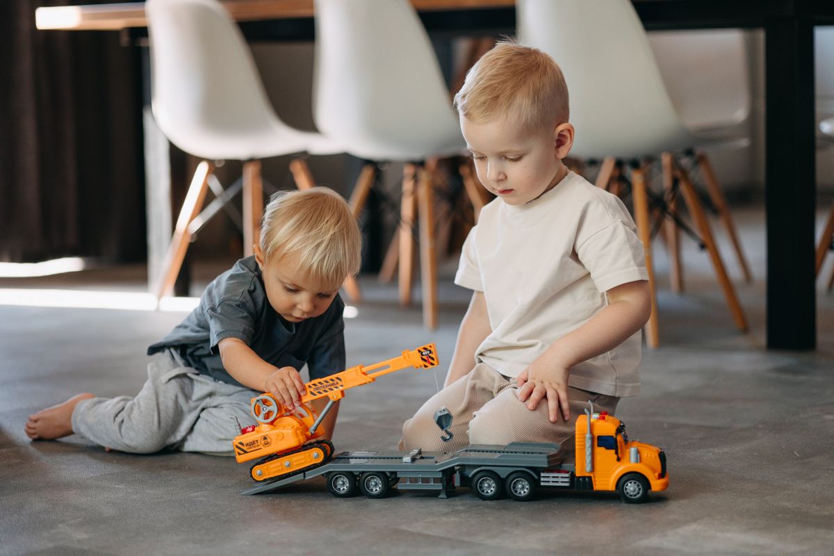 Two young boys enjoy playing with toy trucks indoors in a peaceful setting.