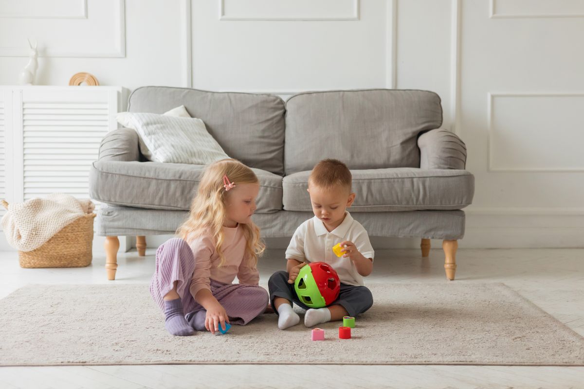 Two children engaged with a colorful toy in a bright, cozy living room setting.