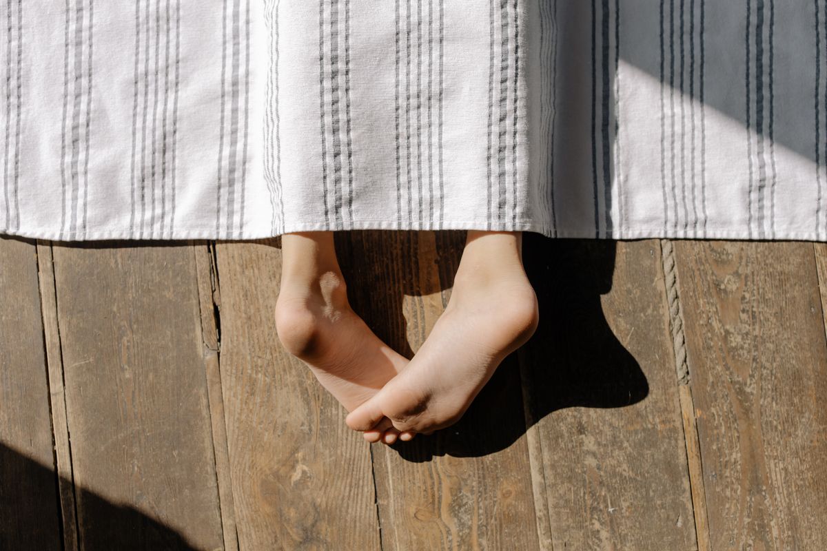 A close-up view of bare feet protruding from a blanket on a wooden floor, capturing a serene moment.