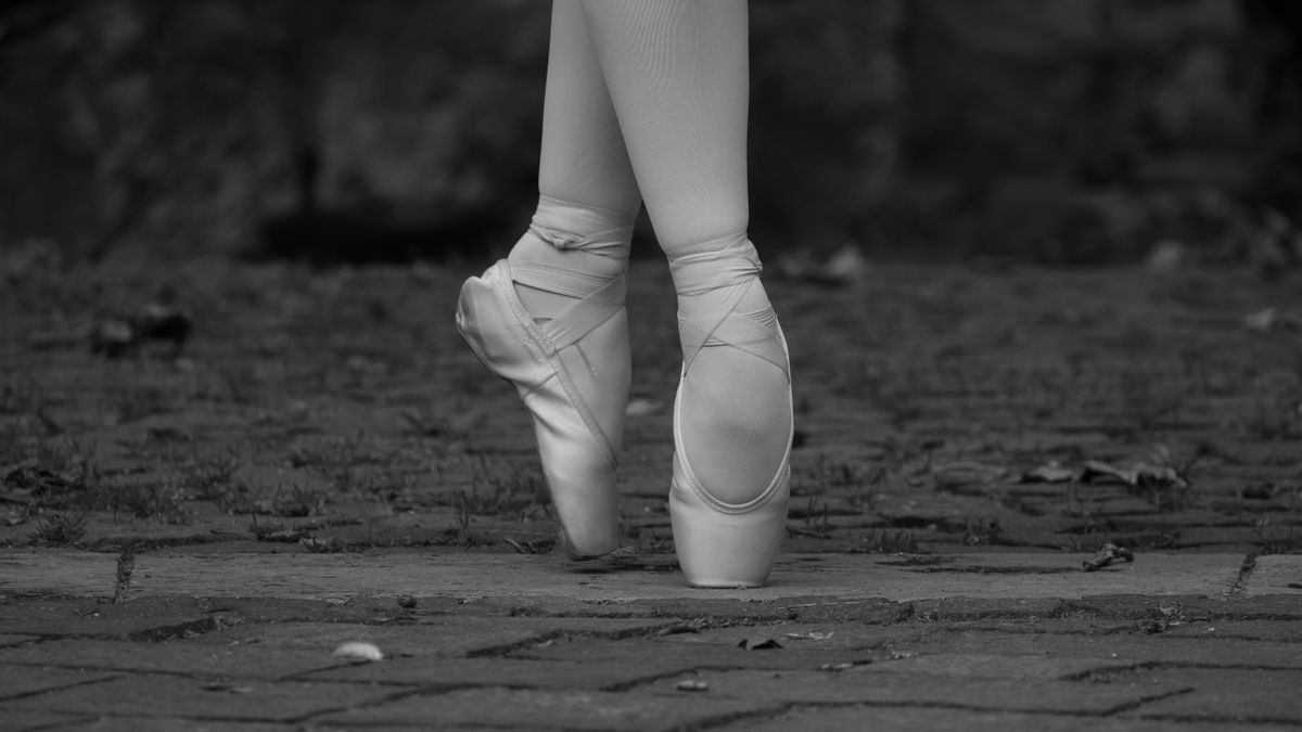 Close-up of ballet dancer's feet in pointe shoes on an outdoor stone pavement, showcasing grace.