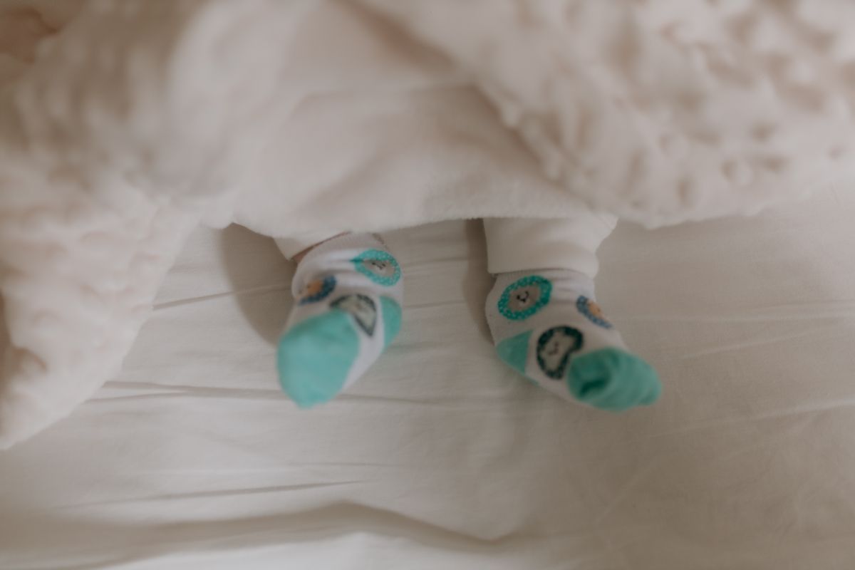 Adorable baby feet wearing cute patterned socks, nestled under a soft white blanket.