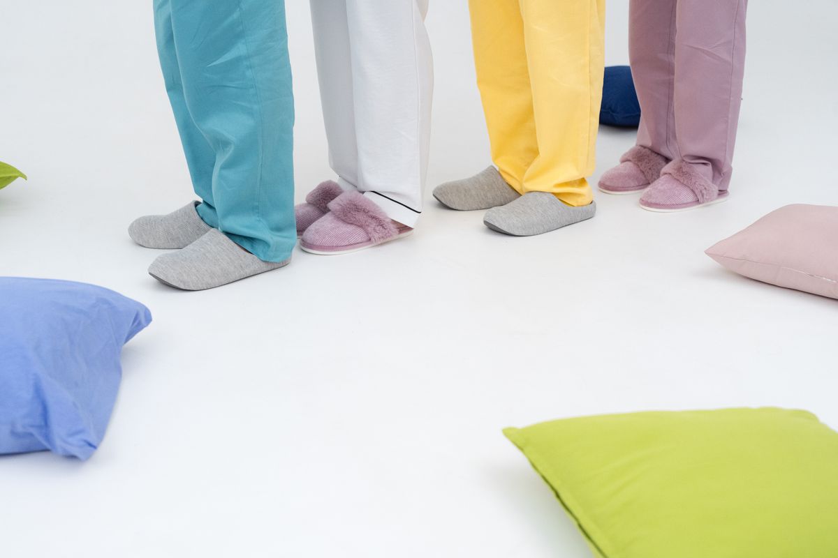 Three people in colorful pajamas and slippers among pillows in a cozy indoor setting.