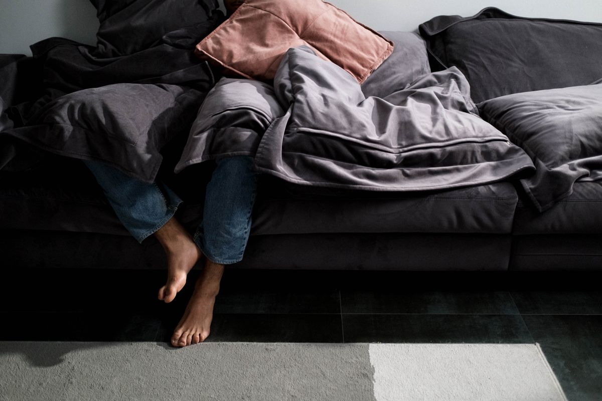 Person lounging on a sofa covered in blankets, showcasing a cozy and relaxed indoor setting.