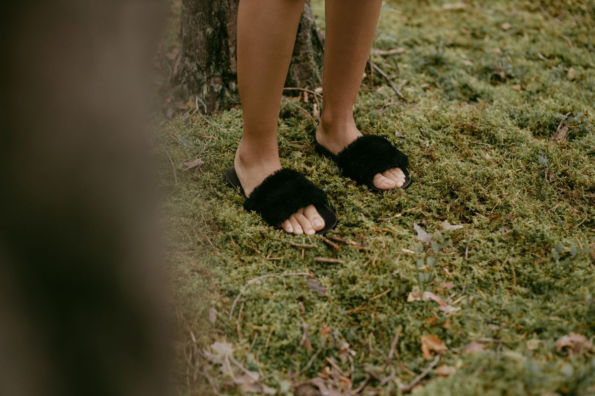 Cozy black fluffy slippers on fresh green moss, outdoor nature scene.