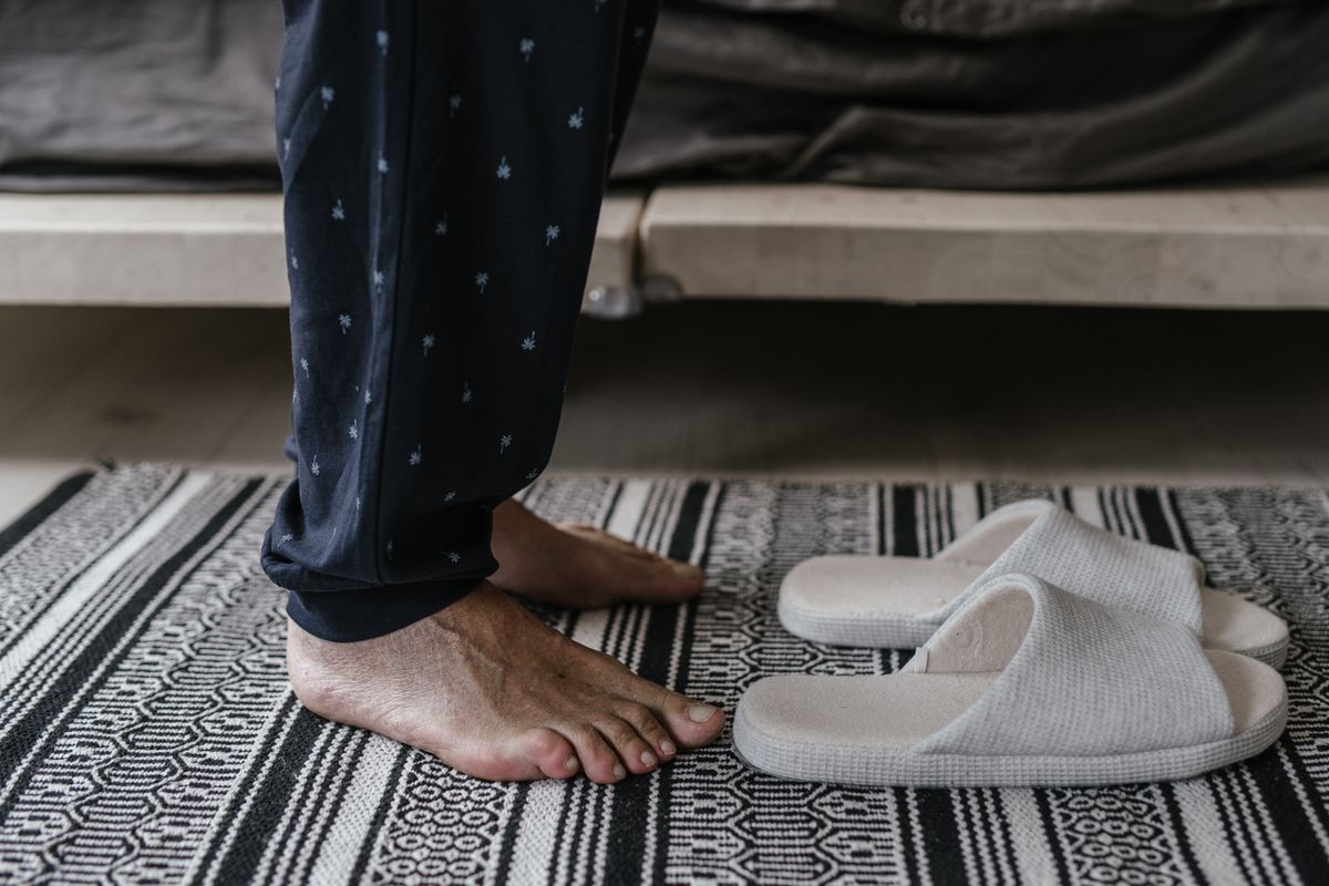 A close-up of bare feet next to slippers on a textured rug. Comfortable home setting.