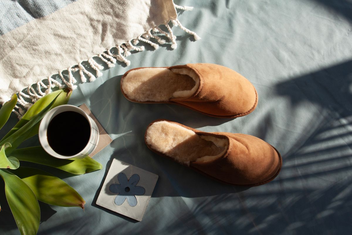 Warm morning scene with slippers, coffee, and natural light on a soft surface.