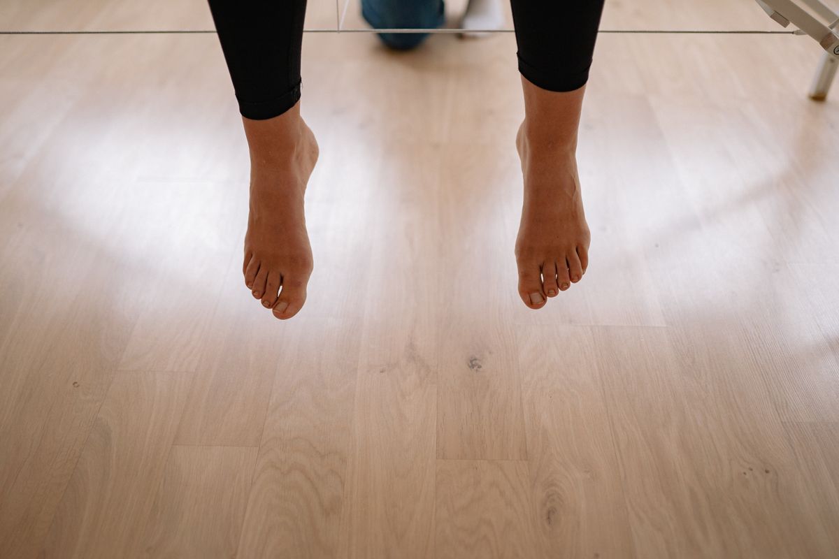 Bare feet hanging above a wooden floor indoors, creating a minimalist and warm scene.