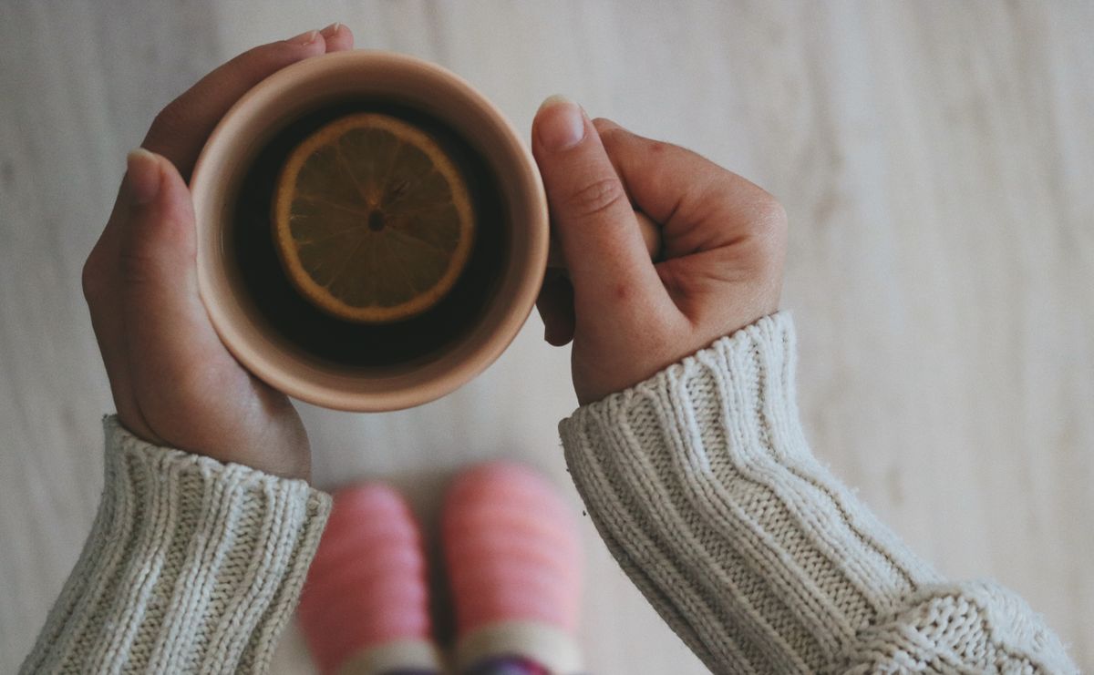 A warm cup of lemon tea held in cozy hands on a winter morning.