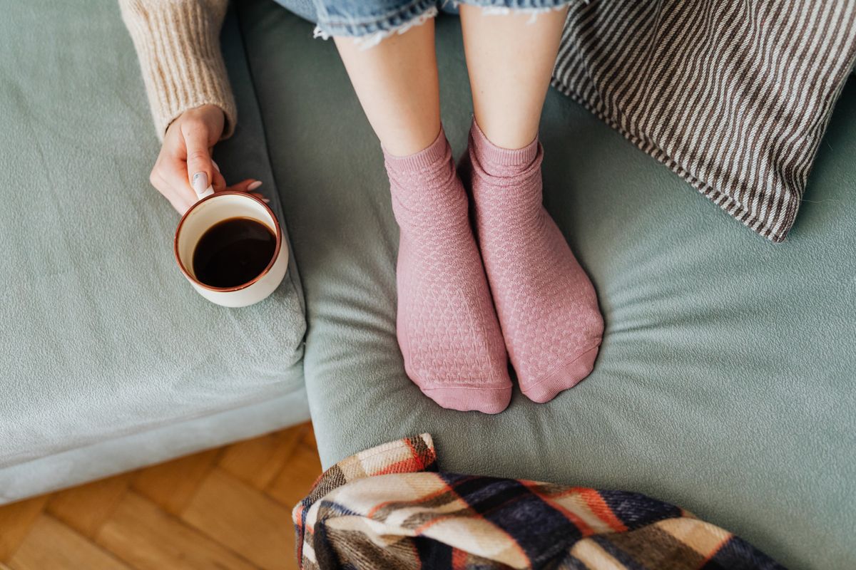 A person relaxing with coffee on a cozy couch wearing pink socks, exuding comfort and warmth.